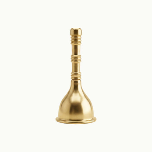 A polished brass menstrual cup with a flared base and ridged neck, standing upright on a clean, light off-white background.