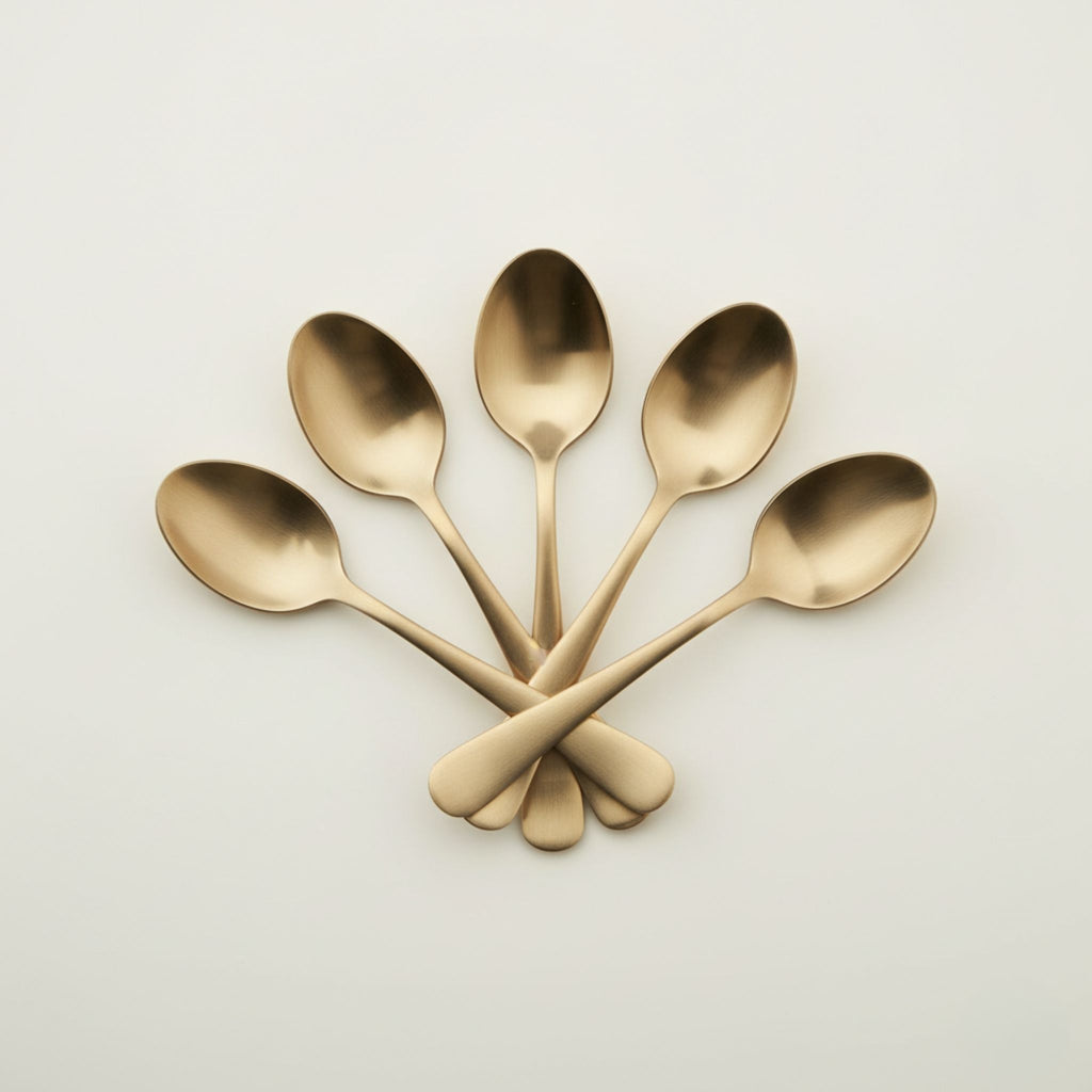 Five polished bronze metal spoons arranged in a fan shape with crossed handles on a clean, light off-white background.