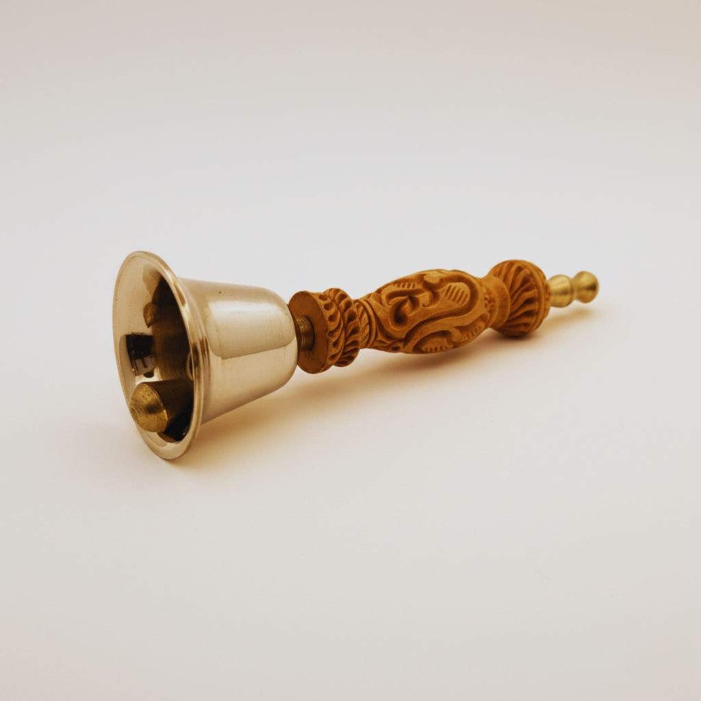 A brass bell with an intricately carved wooden handle, shown on a plain light background.