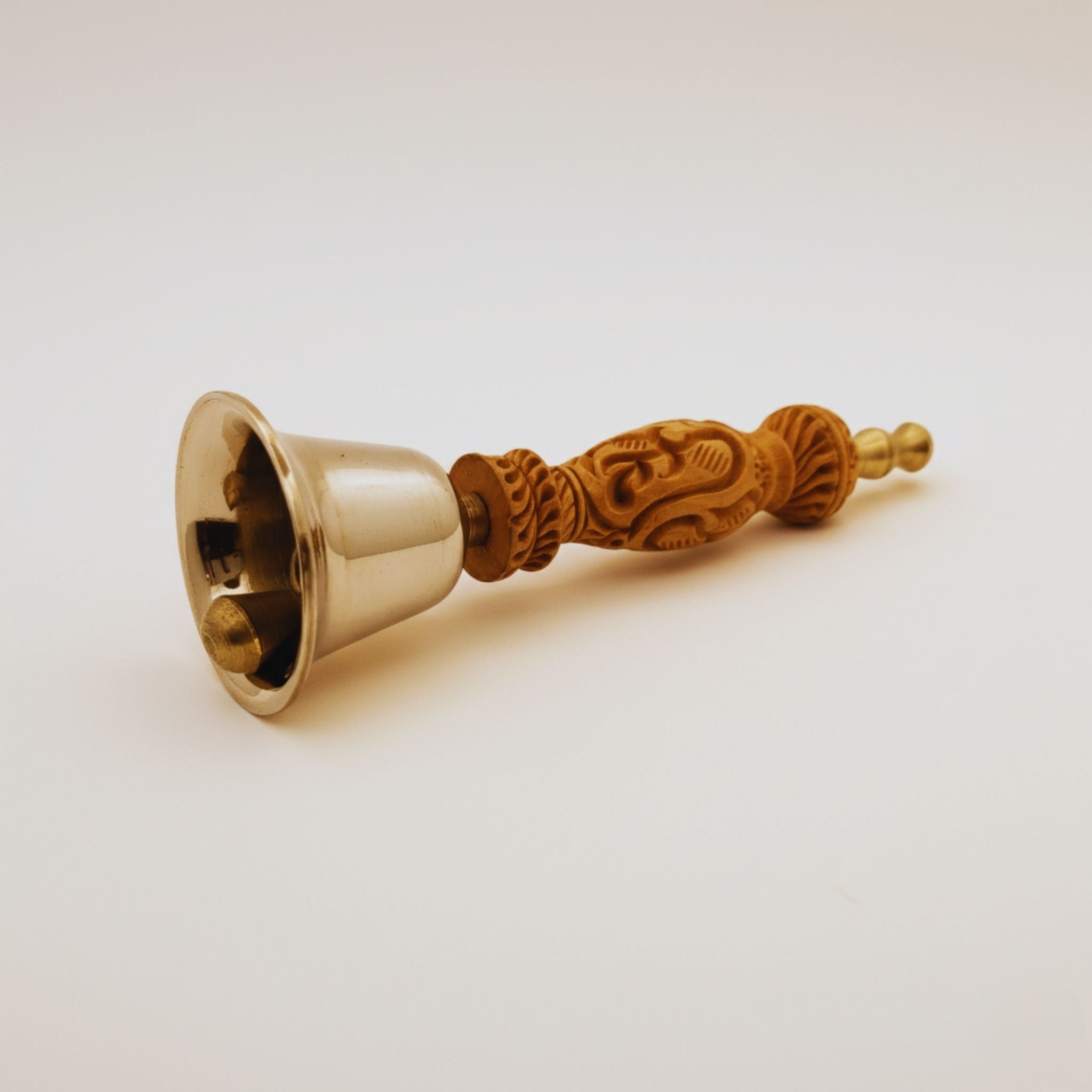 A brass bell with an intricately carved wooden handle, shown on a plain light background.