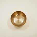 A round metallic bronze bowl with a brushed gold finish, photographed from directly above on a clean, off-white background.