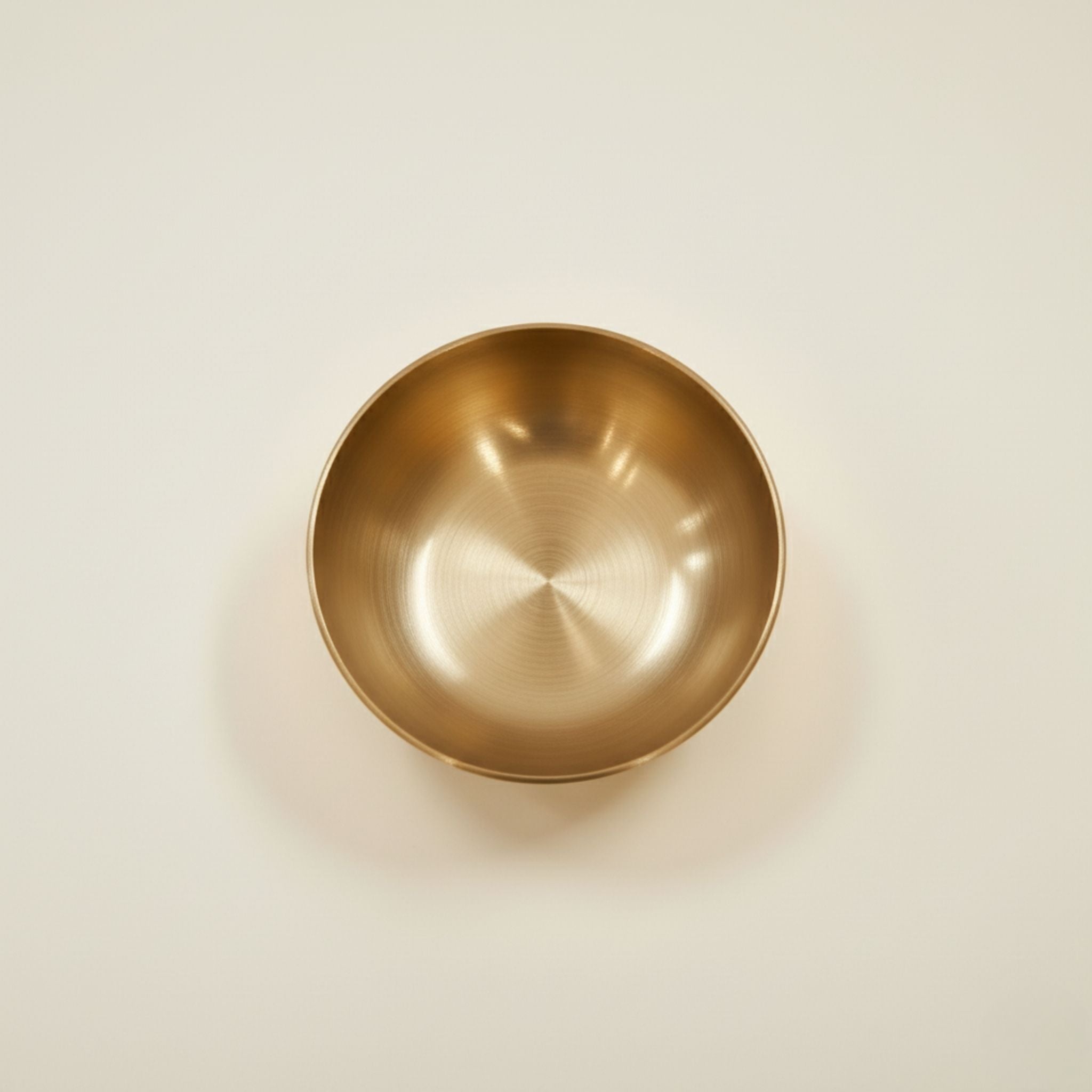 A round metallic bronze bowl with a brushed gold finish, photographed from directly above on a clean, off-white background.