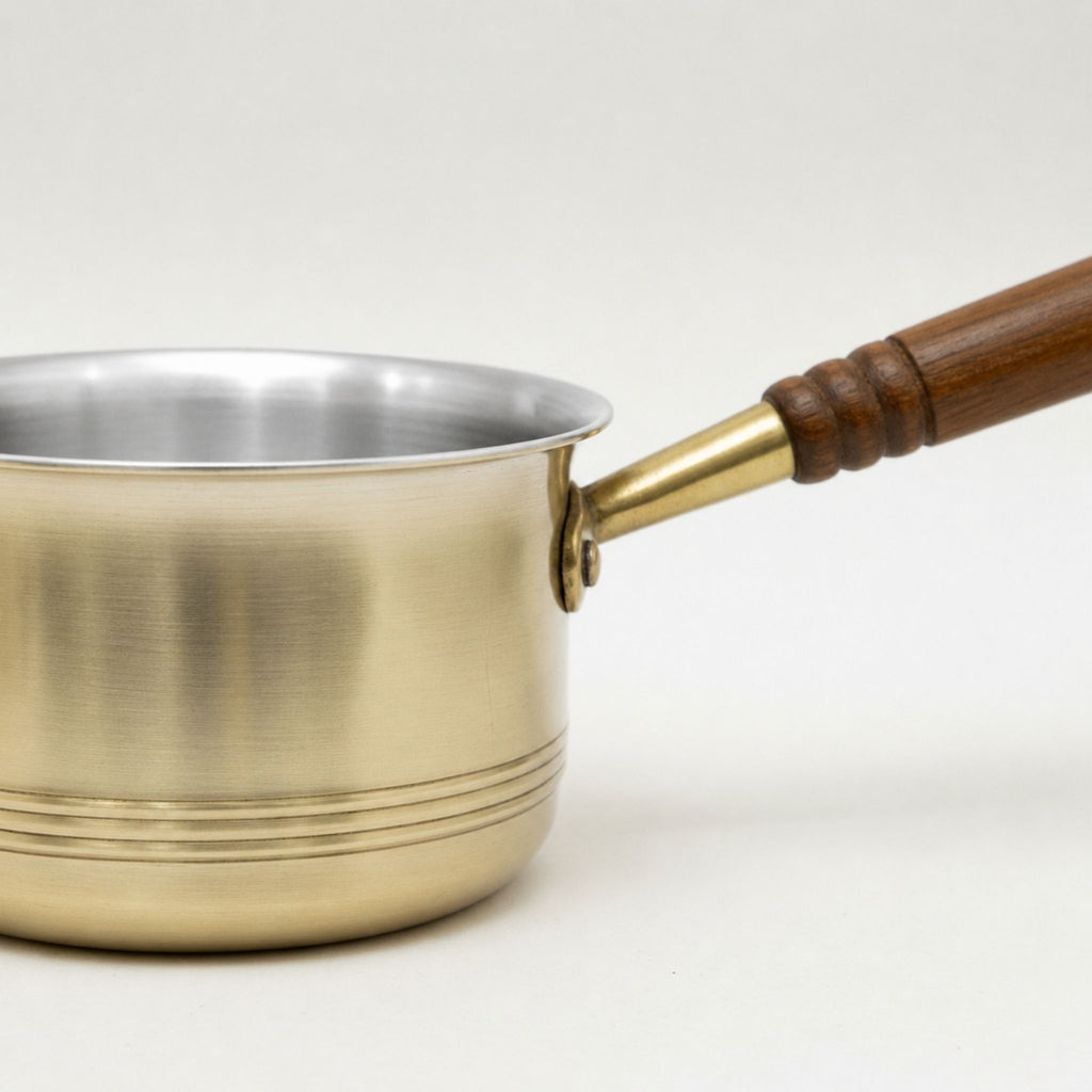 Saucepan with a brass exterior, a polished tin coting interior, and a dark brown wooden handle with a brass ferrule, shown on a plain light background.