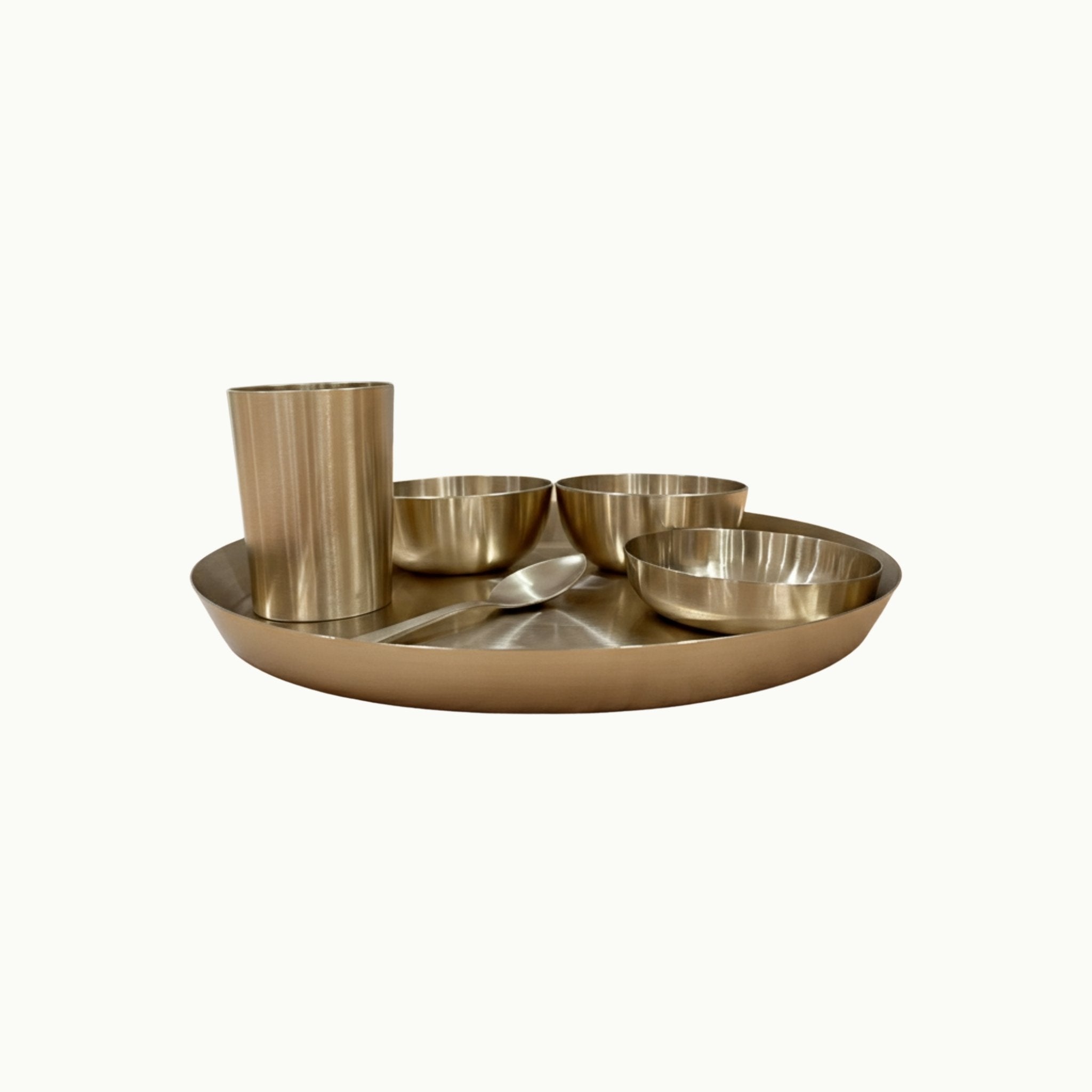 A bronze Indian food tray set with a large round platter, a tall cup, two small bowls, and a spoon, shown on a plain off-white background.
